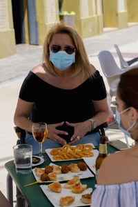 Portrait of mature woman wearing mask sitting at restaurant