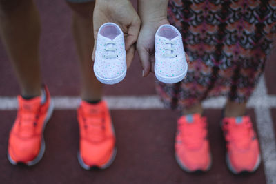 Low section of couple holding baby shoes while standing outdoors