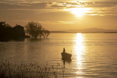 Silhouette man on lake against sky during sunset