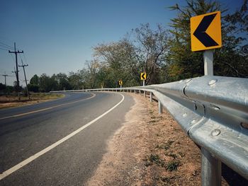 Road sign by trees against sky