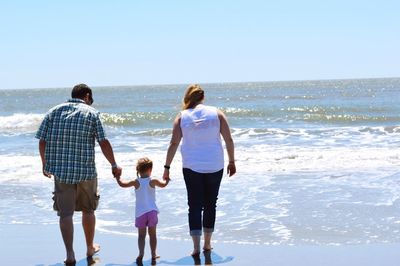 Rear view of parents and daughter walking on beach