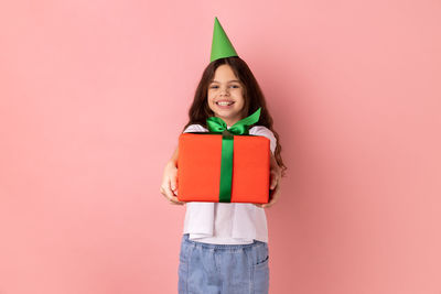 Portrait of smiling young woman standing against pink background