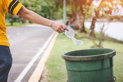 Cropped hand throwing bottle in garbage can