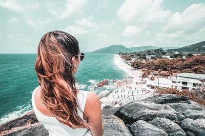 Rear view of woman standing on cliff by sea against sky