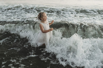 Preschool aged girl splashing in waves at sunset