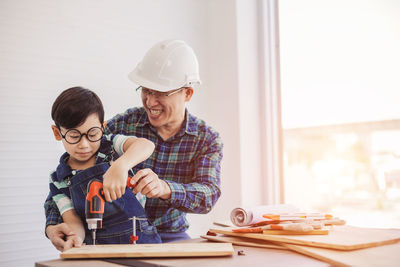 Son drilling wood by father at construction site