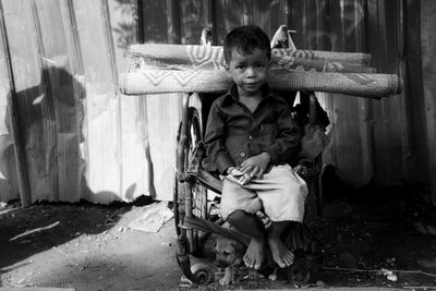 Portrait of boy sitting on old wheelchair with carpet