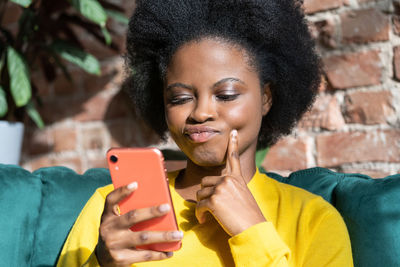 Thoughtful woman using smart phone while sitting home