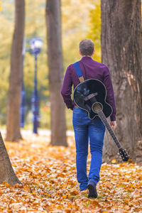 Rear view of young man with guitar walking on field at park during autumn