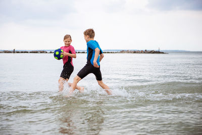 Playful friends playing with soccer ball in sea