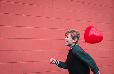 Side view of boy standing against red wall