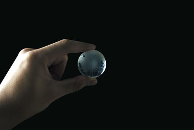Close-up of hand holding crystal ball against black background