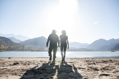 Couple holding hands while walking outdoors with natural landscape of mountains and lake.