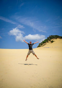 Woman jumping on beach against blue sky