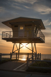 Lifeguard hut at sea shore against sky during sunset