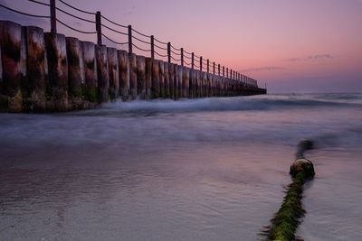 Damaged groyne in sea against sky during sunset