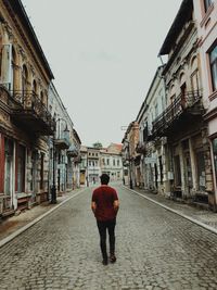 Rear view of man walking on footpath amidst buildings in city