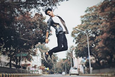 Low angle view of man jumping against trees