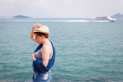 Side view of woman wearing hat while standing at beach