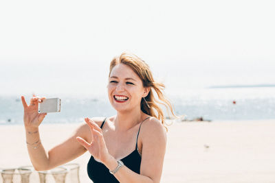 Happy smiling woman holding smart phone while standing on beach