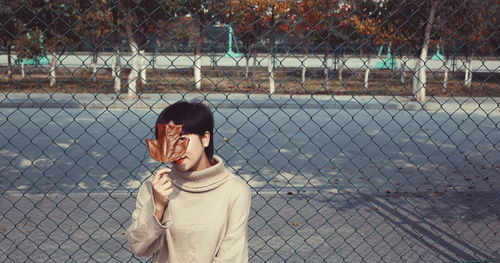 Man standing by chainlink fence against sky in city
