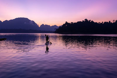 Silhouette man in lake against sky during sunset