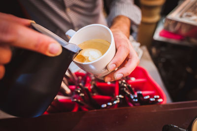 Midsection of barista pouring coffee in cup from container at cafe