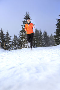 Woman running on snow covered field against clear sky