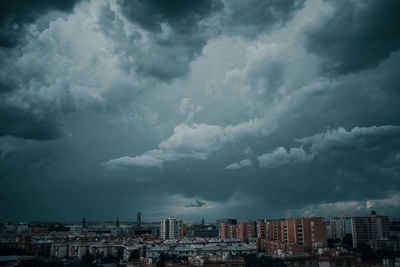 Buildings in city against storm clouds