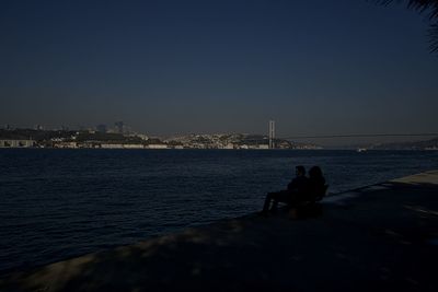 People sitting by sea against clear sky