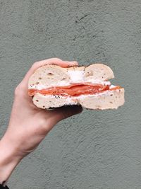 Cropped hand holding burger against wall