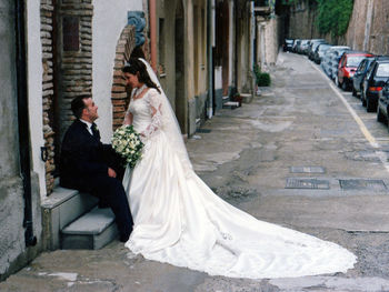 Bride and groom on sidewalk by parked cars in city