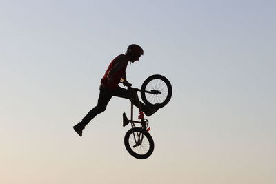 Man with bicycle jumping against clear sky