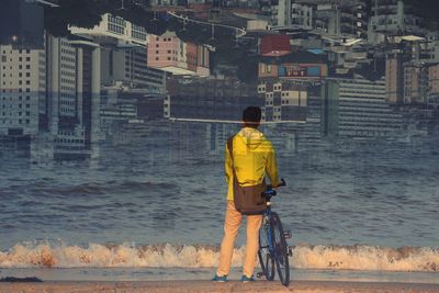 Double exposure of man standing at seashore with cityscape in background