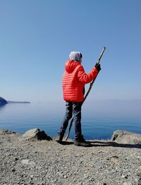 Rear view of boy holding stick while standing against sky