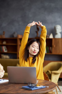 Young woman with arms raised siting at home