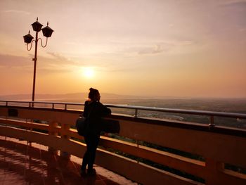 Woman standing by railing against sky during sunset