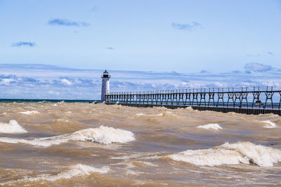 Lighthouse on beach by sea against sky