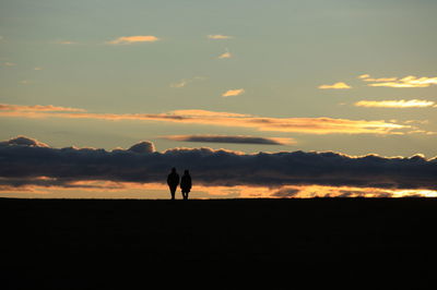 Silhouette couple walking on landscape against sky during sunset