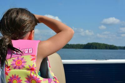 Rear view of girl sitting on boat in lake against blue sky