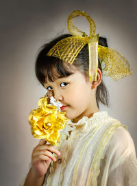 Portrait of woman holding yellow flower against white background