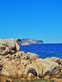 Rock formations by sea against clear blue sky