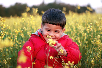 Smiling boy touching flowers on field