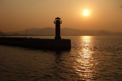 Lighthouse by sea against sky during sunset