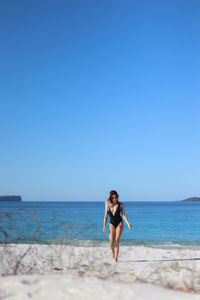 Walking young woman in black bikini and brown sunglasses on beach in eastern australia