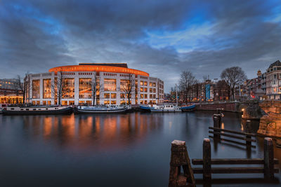 Bridge over river against buildings in city at dusk