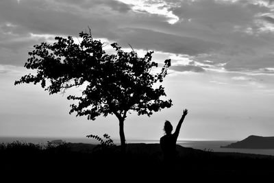 Silhouette person standing by tree on field against sky