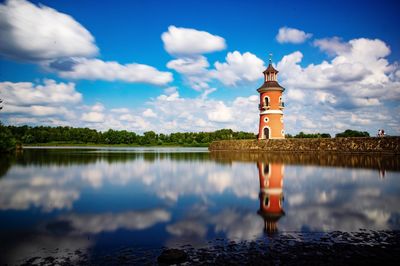 Lighthouse on lake by building against sky