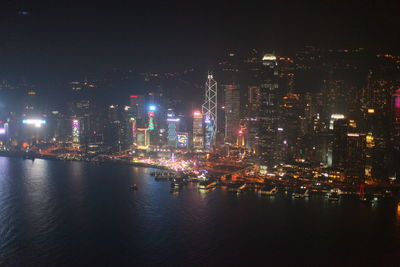 Illuminated city by sea against sky at night