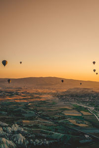 Hot air balloons flying over landscape against sky during sunset